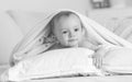 Black and white portrait of toddler boy lying on bed under big blanket Royalty Free Stock Photo