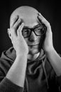 Black and white portrait of a young bald man with black eyeglasses holding his head in his hands Royalty Free Stock Photo