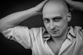 Black and white portrait of a young bald man in a shirt with his hands behind his head and a provocative look Royalty Free Stock Photo