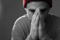 Black and white portrait of a young bearded man in a hat, hands clasped on his face, prays, his eyes down. Studio photo on a gray Royalty Free Stock Photo