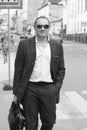 Black and white portrait of a young caucasian man in a business suit and sunglasses holding a suitcase walks across the road. Work Royalty Free Stock Photo