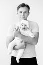 Black-white portrait, young dad with adorable little daughter in the studio. A handsome dad holds the baby in his arms