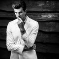 Black-white portrait of young handsome fashionable man in white suit against wooden wall