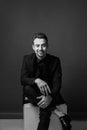 Black and white portrait of a young handsome man in a suit sitting on box, smiling and looking at the camera Royalty Free Stock Photo