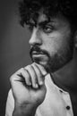 Black and white portrait of a young man with beard and curly hair, holding his chin with his hand and looking thoughtful Royalty Free Stock Photo