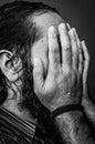 Black and white portrait of a young man with a beard and long hair covering his face with his hands while it is completely wet Royalty Free Stock Photo