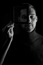 Black and white portrait of a young man holding a frame in front of his face, concept for the uniqueness of individuals Royalty Free Stock Photo