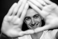 Black and white portrait of a young man in a t-shirt, smiling and looking at the camera through his hands Royalty Free Stock Photo