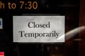 A black and white printed paper closed sign taped to a temporarily shut down business storefront glass window or door due to the