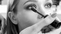 Black and white image of professional makeup artist painting model`s eyes with mascara