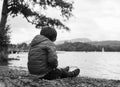 Black and white rear view of lonely kid head down and looking at his feet, Sad child sitting alone by te lake, Bored little boy Royalty Free Stock Photo