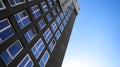 Black and white residential high-rise building with many glass windows standing against background of blue sky and sun Royalty Free Stock Photo