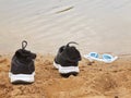 Black and white running shoes and swimming glasses on the orange sand of lake bank. Royalty Free Stock Photo