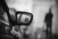 Black-white sad image of the rearview mirror of a car, strewn with raindrops and the silhouette of a passing man Royalty Free Stock Photo