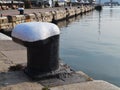 Black and white ship mooring bollard on the edge of the pier in the seaport on an sunny autumn day