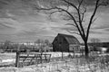 Black and white shot of midwest farm with a barn, bare tree, and fence in snow.