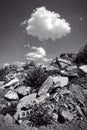 Black and white shot of a pile of rubble under a cloud in the sky.