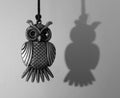 Black and white shot of a small metallic owl pendant near the wall with its shadow Royalty Free Stock Photo