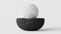 A black and white speckled sphere rests on a black speckled bowl. Royalty Free Stock Photo