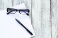 Black and white still life: opened blank notepad, notebooks, pen, glasses.