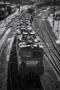 Black and white street photo with a passing large train. Front and top view of an electric locomotive pulling a freight train.