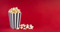 Black white striped carton bucket with tasty cheese popcorn, isolated on red background
