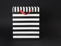 Black and white stripped gift-bag with red satin handles, on a black background.