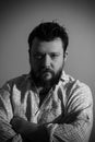 Black and white studio portrait of a brutal bearded man with a serious face in a light shirt holds his hands folded over his chest Royalty Free Stock Photo