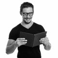 Studio shot of young happy man smiling while reading book with eyeglasses isolated against white background Royalty Free Stock Photo