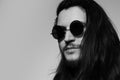 Black and white studio portrait of young serious man with long hair,  wearing round sunglasses. Copy space concept. Royalty Free Stock Photo