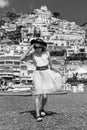 Black and white. Summer fashion. A girl in a white dress, sunglasses and a hat stands on the beach in Positano. View of houses and Royalty Free Stock Photo