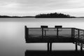 Black and white tranquil scenery of a lake with pier and two chairs