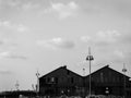 Black and white urban view of two roof tops of big buildings by the sea port, boat houses with tall city lamps in front, under