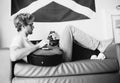 Black and white vintage image style middle shot of young teenager lying on sofa and playing on guitar in teen room