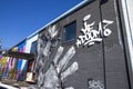 A black and white wall mural of MF Doom on the side of a brick building in Little Five Points surrounded by parked cars