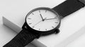 Black and white watch with a white face sits on a white surface Royalty Free Stock Photo