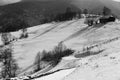 Black and white winter landscape of houses and trees on snowy hills