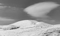 Black and white winter landscape of a snow caped mountain and a huge white cloud floating above it