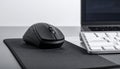 Black wireless computer mouse on a black mousepad next to a white keyboard and laptop on a gray desk Royalty Free Stock Photo