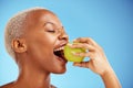 Black woman, apple and bite in diet, nutrition or health and wellness against a blue studio background. Face of African