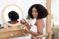 Black woman applying makeup in front of mirror, sitting at dressing table with eye shadow palette, smiling at camera Royalty Free Stock Photo