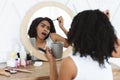 Black woman applying makeup in hurry, drinking coffee and talking on cellphone Royalty Free Stock Photo