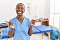 Black woman with braids working at pain recovery clinic smiling confident pointing with fingers to different directions