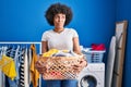 Black woman with curly hair holding laundry basket smiling looking to the side and staring away thinking