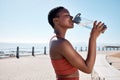 Black woman, drinking water or bottle in fitness workout, training or exercise by beach, ocean or sea in summer location Royalty Free Stock Photo