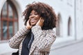 Black woman, earphones and listening to music in the city streets with smile for entertainment. Happy African American