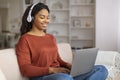 Black woman enjoying music with headphones while working on laptop at home Royalty Free Stock Photo