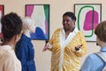 Black woman giving tour to group of teenagers in art gallery