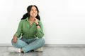 Black woman looks aside with smile, sitting near white wall Royalty Free Stock Photo