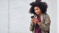 Black woman, phone and earphones in city, texting and smile for flirt chat, online date or meme on app. Young gen z girl